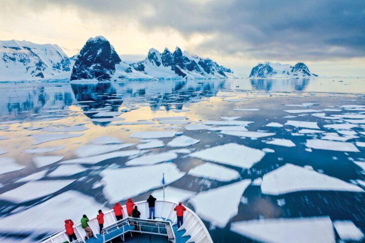 Passengers watch from the bow of a cruise ship as it goes through ice.