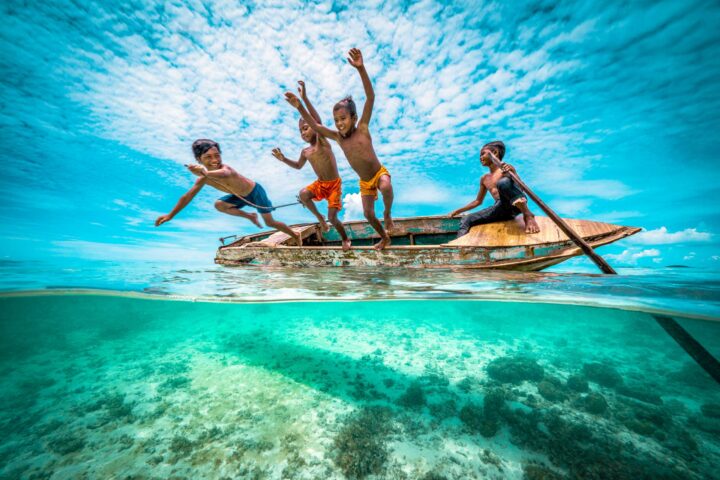 A group of kids jumping into the water from a canoe.