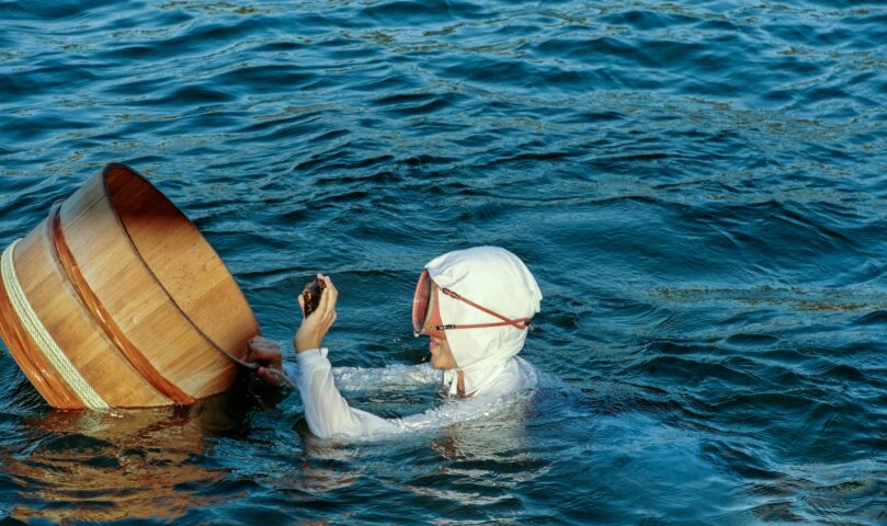 A woman wearing traditional white clothing, showing an abalone during a demonstration in Toba Bay, Mikimoto Pearl Island.